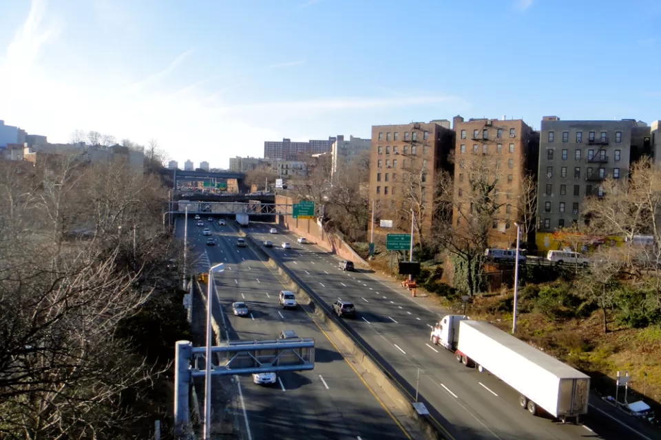 A view of the Cross Bronx Expressway, an elevated highway that allows cars to drive past apartment buildings.